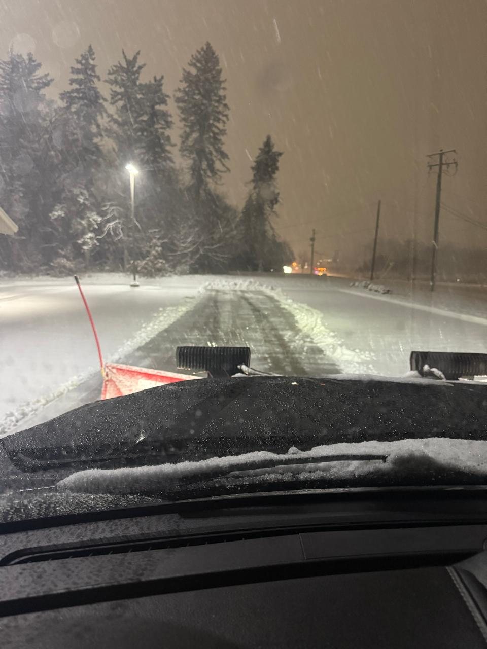 View from a plow truck clearing a parking lot at night during heavy snowfall